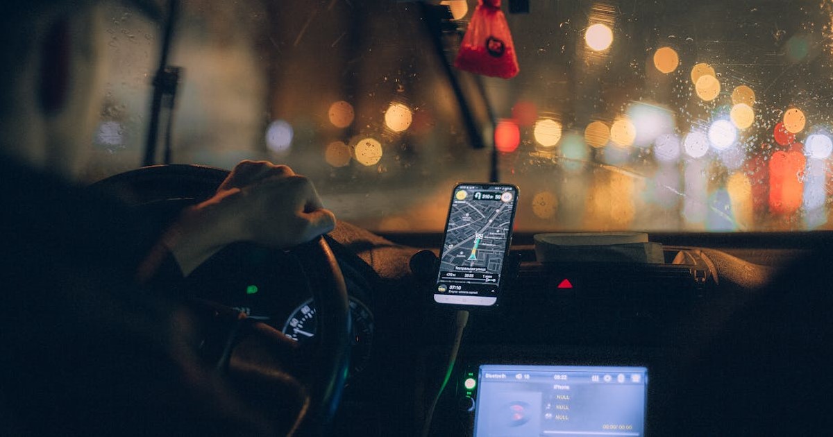 Aplikasi navigasi anti macet: Seseorang sedang melihat peta rute jalan raya digital di layar smartphone yang terpasang di dashboard mobil