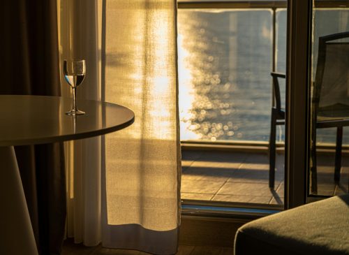 Ilustrasi pemandangan kamar hotel mewah dengan dekorasi estetik yang menghadap ke laut Makassar saat sunset.
