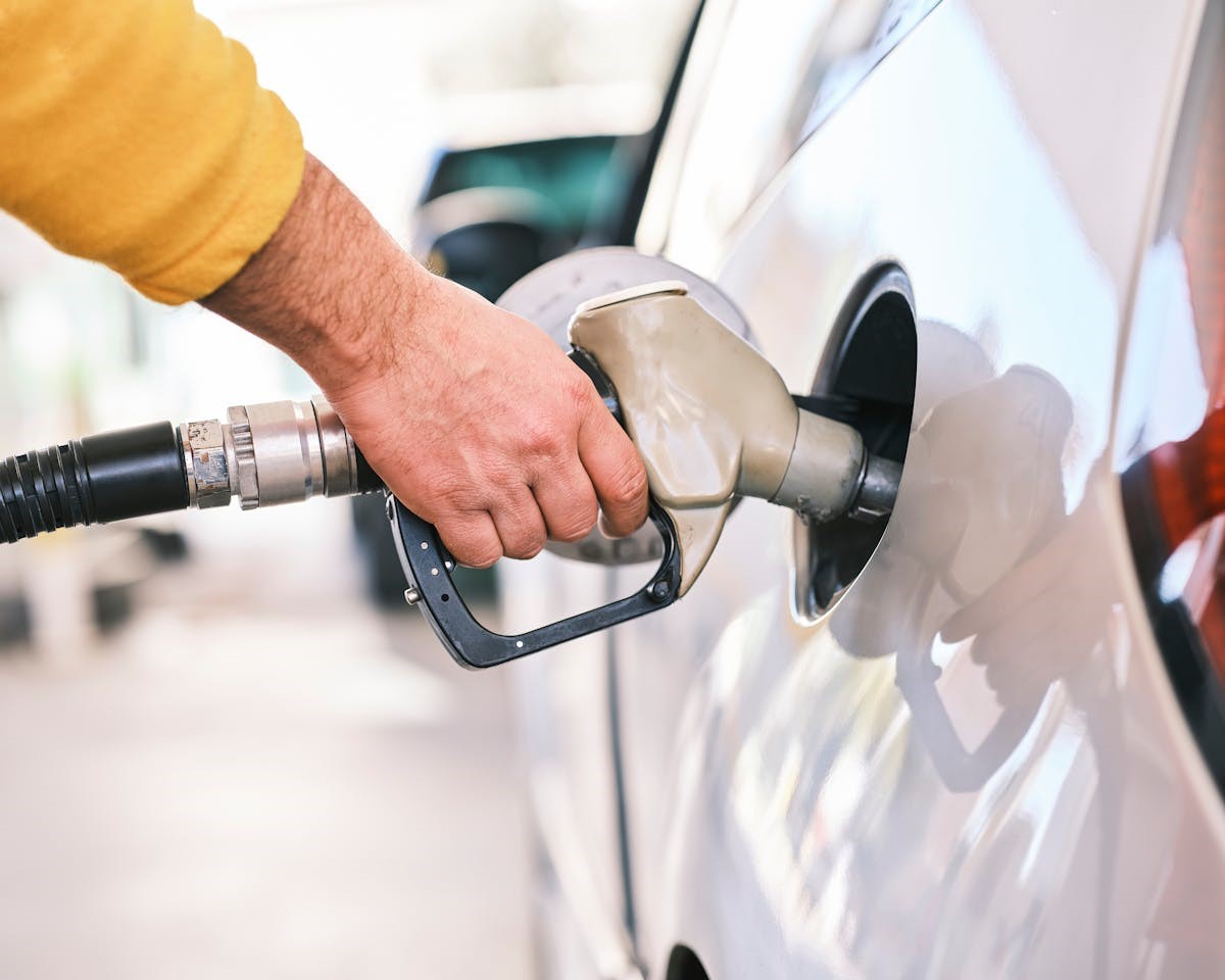 Seseorang sedang memegang nozzle dispenser bensin di SPBU perkotaan modern, Tips hemat bensin mobil ini bisa diterapkan dengan mudah.