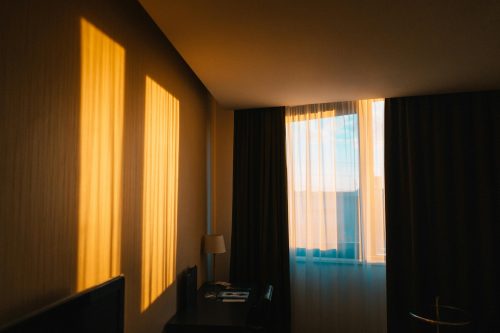 Ilustrasi interior kamar hotel butik lantai atas dengan jendela besar menghadap ke arah laut pantai Makassar.