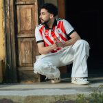 OOTD jersey bola: Seorang pria muda tampil modis mengenakan jersey vintage yang dipadukan dengan celana jeans longgar dan sepatu kets retro