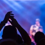Panduan konser musik 2026: Ilustrasi suasana panggung konser musik besar di malam hari dengan gemerlap lampu sorot dramatis dan lautan penonton