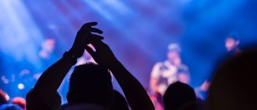 Panduan konser musik 2026: Ilustrasi suasana panggung konser musik besar di malam hari dengan gemerlap lampu sorot dramatis dan lautan penonton