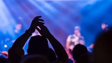 Panduan konser musik 2026: Ilustrasi suasana panggung konser musik besar di malam hari dengan gemerlap lampu sorot dramatis dan lautan penonton