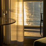 Ilustrasi pemandangan kamar hotel mewah dengan dekorasi estetik yang menghadap ke laut Makassar saat sunset.