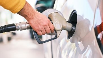 Seseorang sedang memegang nozzle dispenser bensin di SPBU perkotaan modern, Tips hemat bensin mobil ini bisa diterapkan dengan mudah.