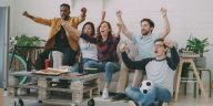 Tips nonton bareng : Sekelompok anak muda sedang bersorak gembira menonton pertandingan bola di depan layar televisi ruang tamu