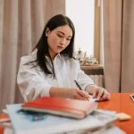Seseorang mencatat poin evaluasi kerja mingguan di buku catatan meja kantor