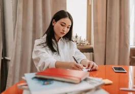 Seseorang mencatat poin evaluasi kerja mingguan di buku catatan meja kantor