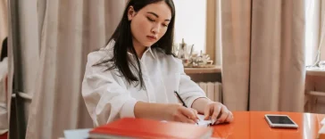 Seseorang mencatat poin evaluasi kerja mingguan di buku catatan meja kantor