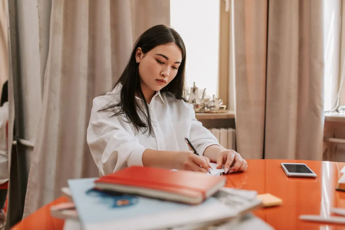Seseorang mencatat poin evaluasi kerja mingguan di buku catatan meja kantor