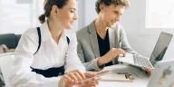 Ilustrasi dua profesional saling tersenyum dan menjaga relasi profesional di ruang istirahat kantor